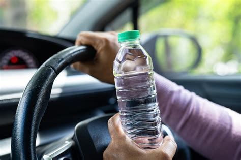 Motorista asiática segurando garrafa de água potável enquanto dirige um