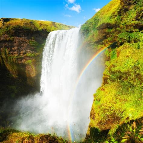 Cachoeira skogafoss arco íris e falésias verdes sul da islândia