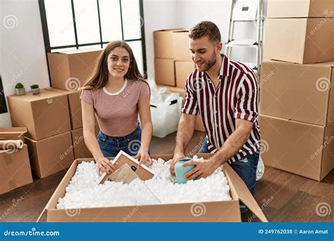 Young Caucasian Couple Smiling Happy Unboxing Cardboard Box At New Home