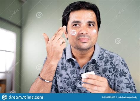 Handsome Smiling Young Man Applying Cream Or Anti Aging Moisture On