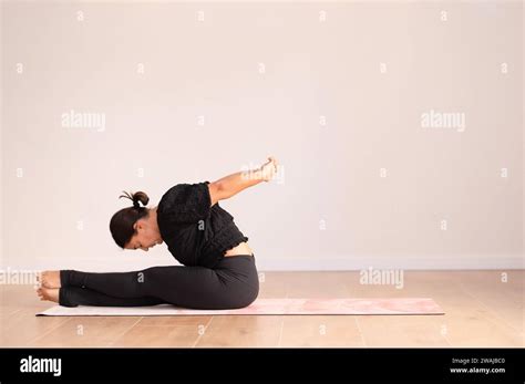 Concentrated Lady In Black Activewear Sitting On Mat Bending Forward