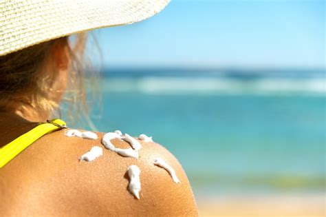 Premium Photo | Back view of young woman tanning at the beach with sunscreen cream in sun shape ...