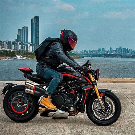 A Man Riding On The Back Of A Motorcycle Down A Street Next To A Body