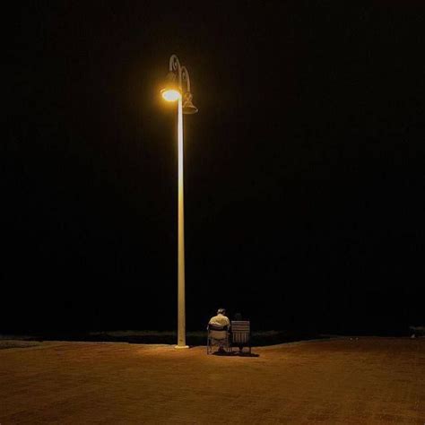 Two People Are Sitting On A Bench Under A Street Light At Night In The