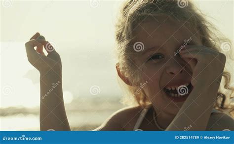 Portrait Of A Happy Blonde Little Girl Playing With Pebble On The Beach