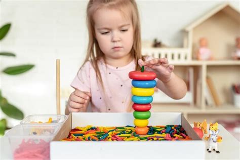 Une Petite Fille Jouant Avec Une Pyramide En Bois Et Des Pâtes Colorées