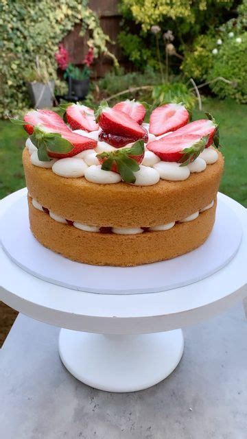 A Cake With Strawberries On Top Is Sitting On A White Pedestal In The