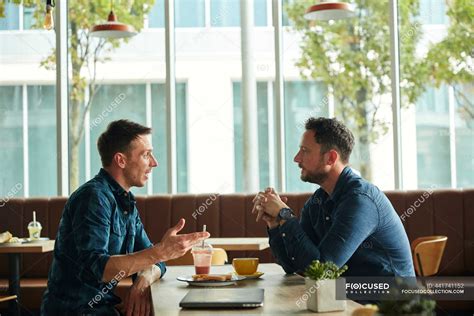 Two Men Sitting In A Cafe Talking Having A Meeting People Real