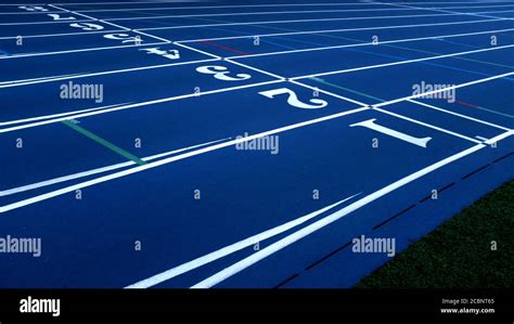 Blue Running Track With White Lane Numbers And Green Grass Stock Photo