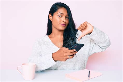 Bella Joven Latina Con El Pelo Largo Usando Un Smartphone Sentado En La Mesa Con La Cara Enojada