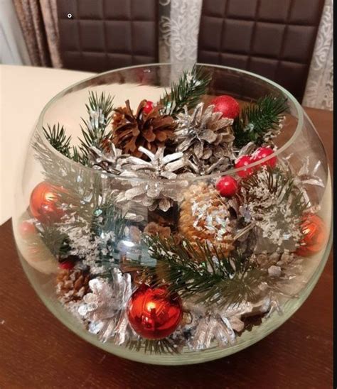 A Glass Bowl Filled With Christmas Decorations And Pine Cones On Top Of