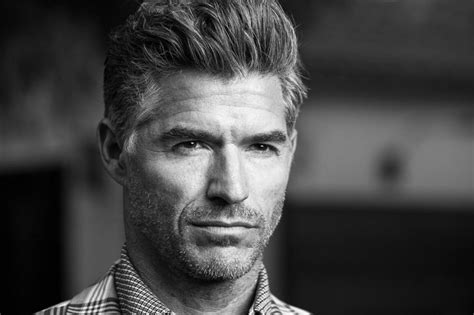 A Black And White Photo Of A Man Wearing A Plaid Shirt Looking At The Camera