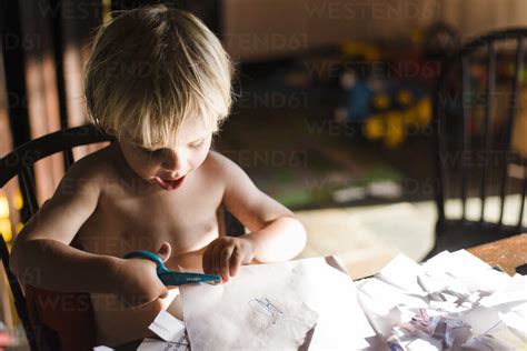 High Angle View Of Shirtless Boy Cutting Papers With Scissors While