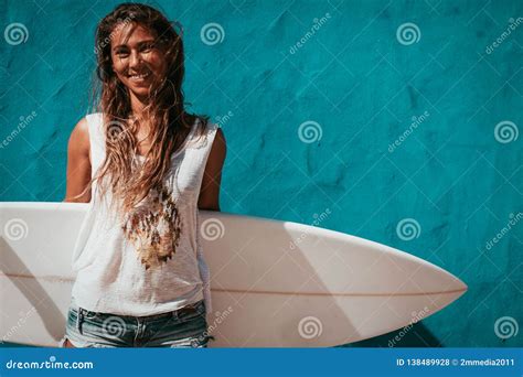 Happy Surfer Girl With Surfboard In Front Of Blue Wall Stock Photo