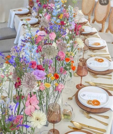 A Long Table Is Set With Flowers And Gold Place Settings For An Elegant