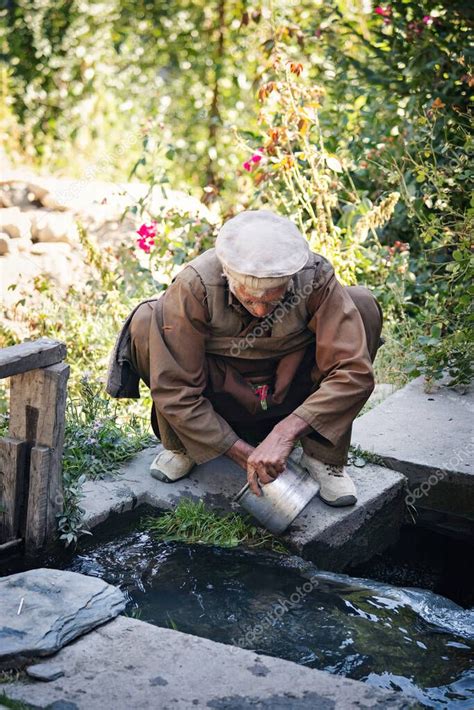 Hombre paquistaní del pueblo Kalash lavando platos en el río en el