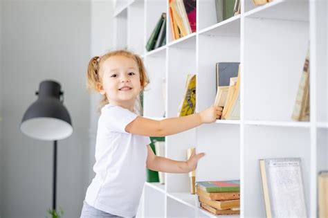 Uma Pequena Menina Loira Tira Um Livro Em Uma Biblioteca Brilhante Em