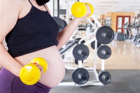 Mulher grávida anônima exercitando levantamento de halteres em uma sala