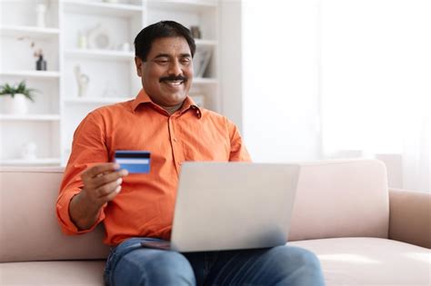 Premium Photo Mature Indian Man Using Laptop And Credit Card At Home