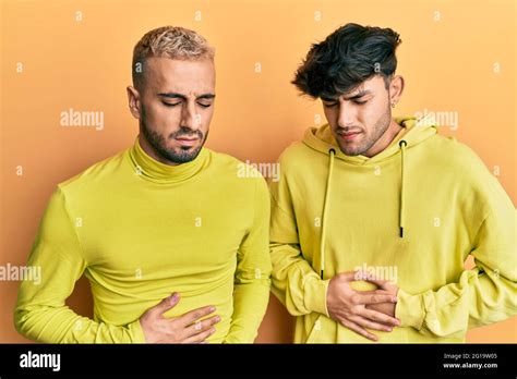 Pareja homosexual gay de pie juntos usando ropa amarilla con la mano en el estómago porque