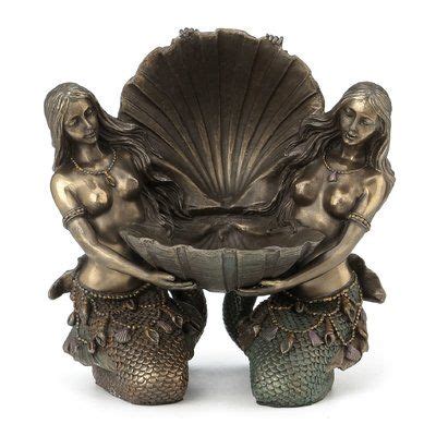 Two Mermaid Figurines Sitting On Top Of Each Other Holding A Large Seashell