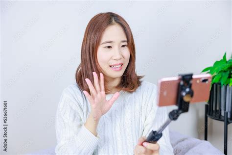 携帯電話のカメラに向かって笑顔で手を振る女性 Stock Foto Adobe Stock