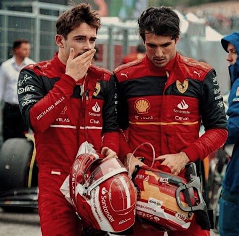 Two Men In Red Racing Suits Standing Next To Each Other