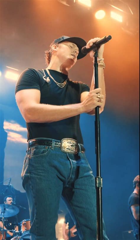 a man in black shirt and jeans holding a microphone with his right hand on stage