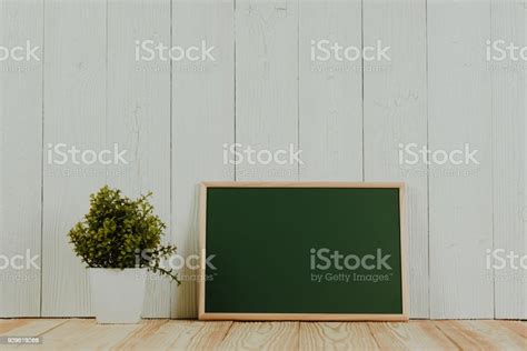 Blank Green Chalkborad With Wood Frame And Little Decorative Tree In White Vase On Wooden Table