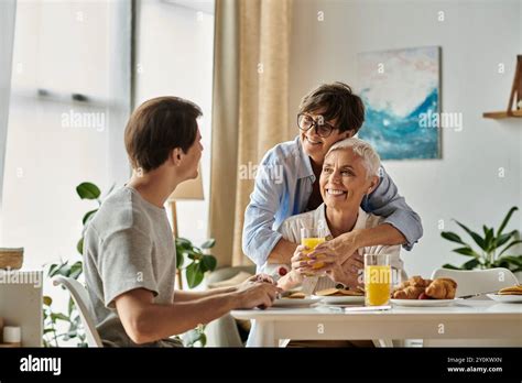 Lesbian Parents And Their Adult Son Share A Warm Breakfast Filled With Laughter And Love Stock