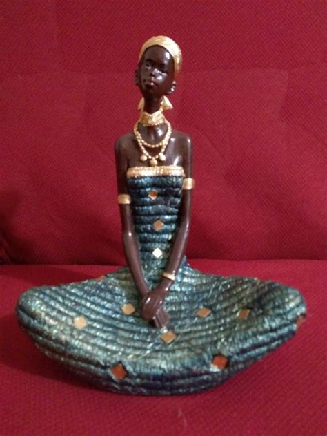 An African Woman Figurine Sitting On Top Of A Blue And Green Dress With