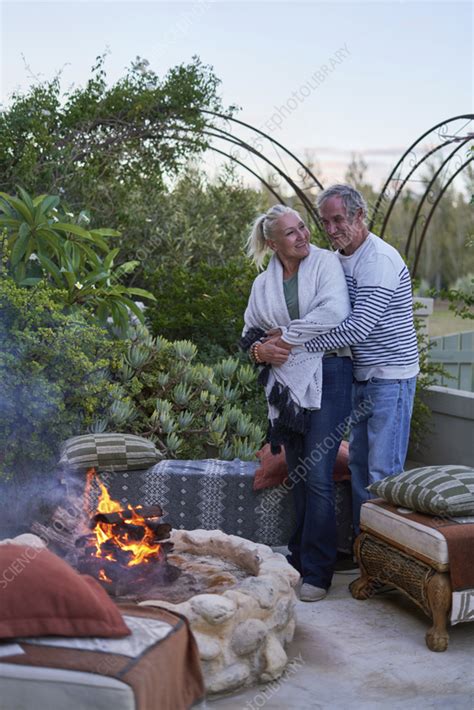 Senior Couple Hugging By Fire Pit On Garden Patio Stock Image F037