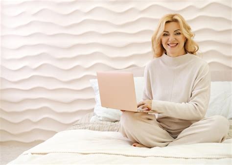 Premium Photo A Beautiful Slender Mature Woman Is Sitting On A Bed With A Laptop In A Beige