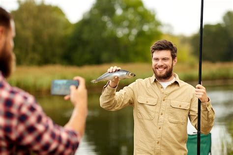 Premium Photo Friend Photographing Fisherman With Fish At Lake