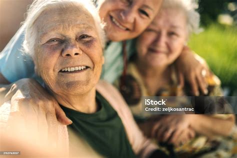 Elderly Woman In Wheelchair With Nurse Outdoors Smiling And Taking