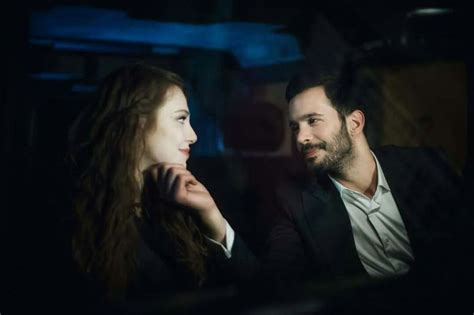 A Man And Woman Sitting Next To Each Other In The Dark Looking At Each