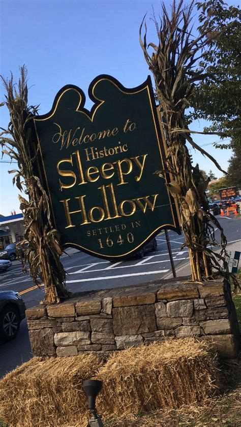 A Welcome Sign To Sleepy Hollow In Front Of A Parking Lot With Hay Bales