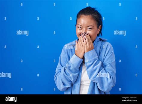 Asian Young Woman Standing Over Blue Background Laughing And Embarrassed Giggle Covering Mouth