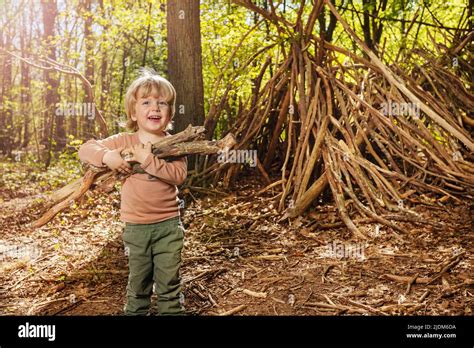 Boy With Brushwood Pile In The Forest Build Hut Of Branches Stock Photo