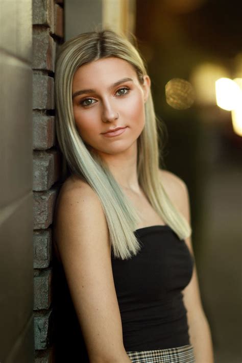 A Woman With Long Blonde Hair Leaning Against A Brick Wall And Looking