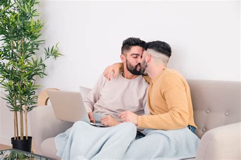 Giovani coppie gay romantiche che si siedono sul sofà che si bacia Foto Gratis