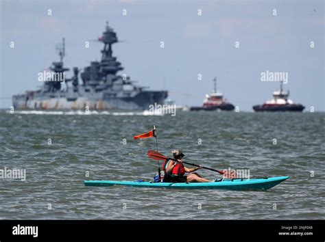 A Woman Paddles A Kayak Along The Texas City Dyke As The Uss Texas