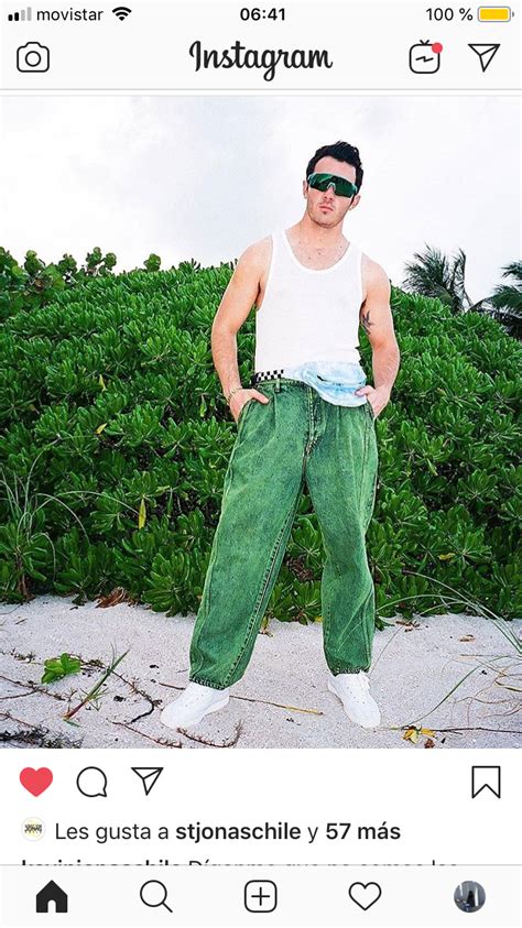 A Man Wearing Green Pants And Sunglasses Standing In Front Of Bushes