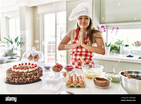 Beautiful Young Brunette Pastry Chef Woman Cooking Pastries At The Kitchen Praying With Hands