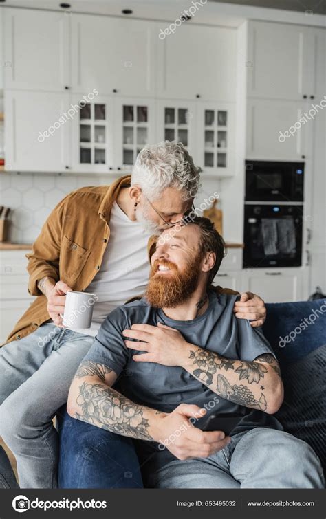 Mature Gay Man Holding Coffee Kissing Cheerful Partner Smartphone