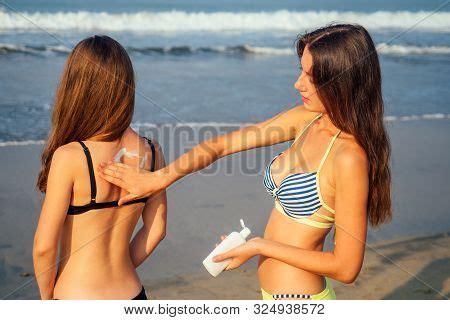 Two Sexy Girls Apply Each Other Sunscreen On Their Backs On The Beach