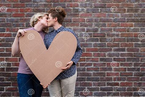 Affectionate Young Lesbian Couple Kissing And Holding A Heart Outside