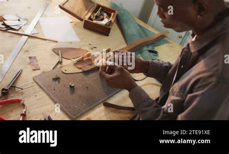 Focused African American Craftsman Using Tools To Make A Belt In