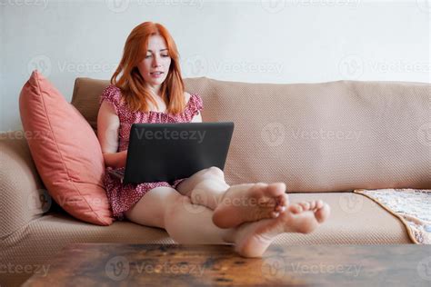 Young Woman With Laptop Working From Home Sitting On Sofa With Feet On