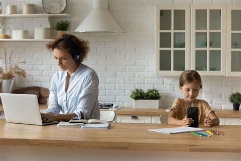 Young Mother Working On Computer While Daughter Playing Phone Stock